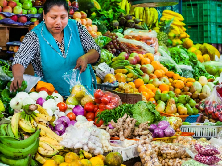La imagen muestra a una mujer vendiendo frutas y verduras en un mercado